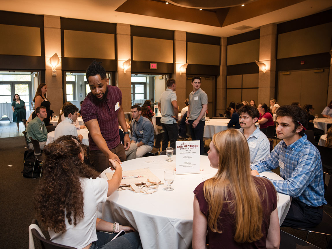 A man shakes hands with a college student during a roundtable networking event
